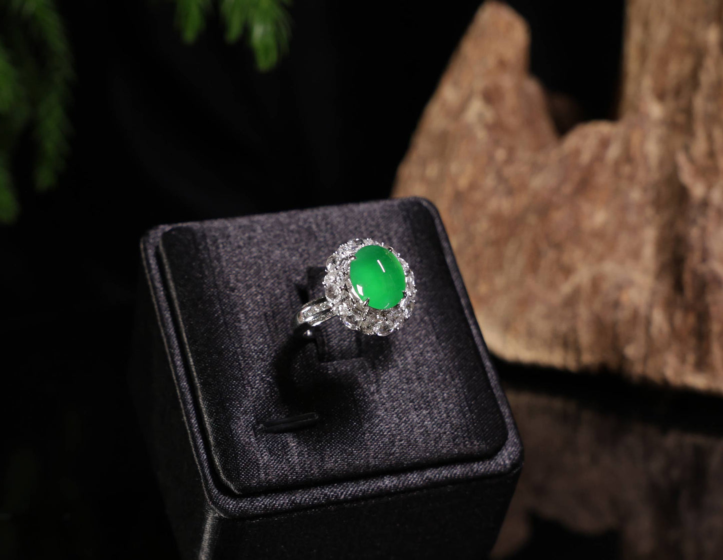 Green gemstone ring on a black cushion with a blurred natural background