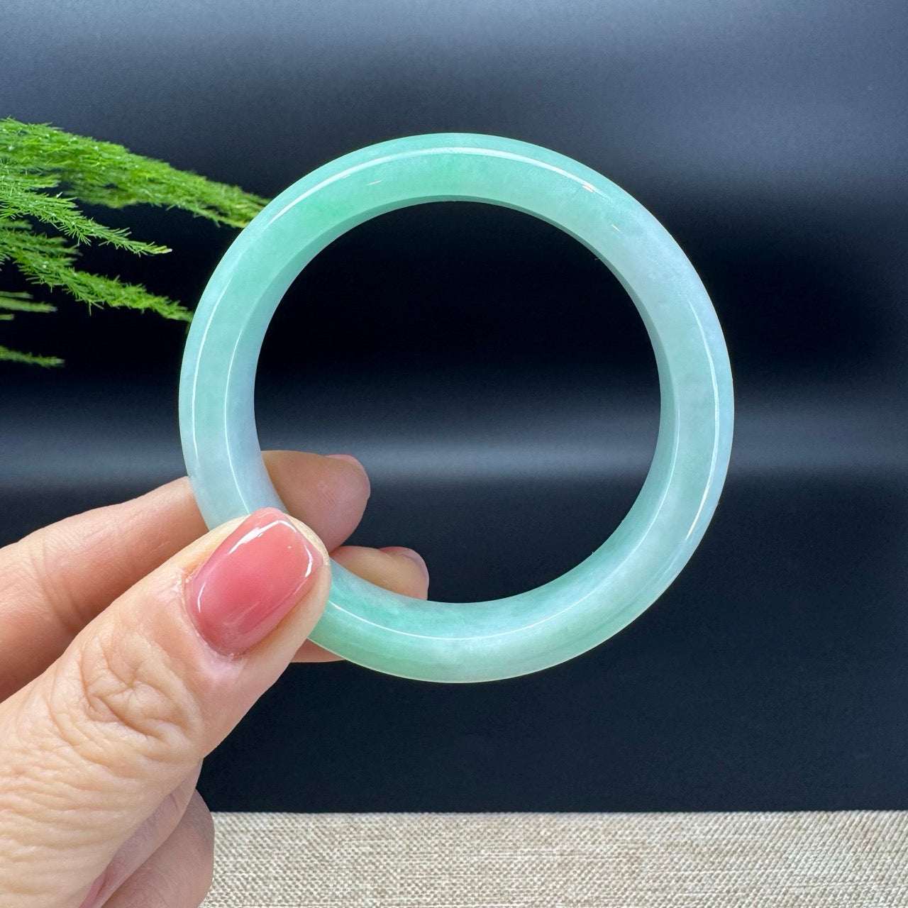 Hand holding a light green jade bracelet against a dark background